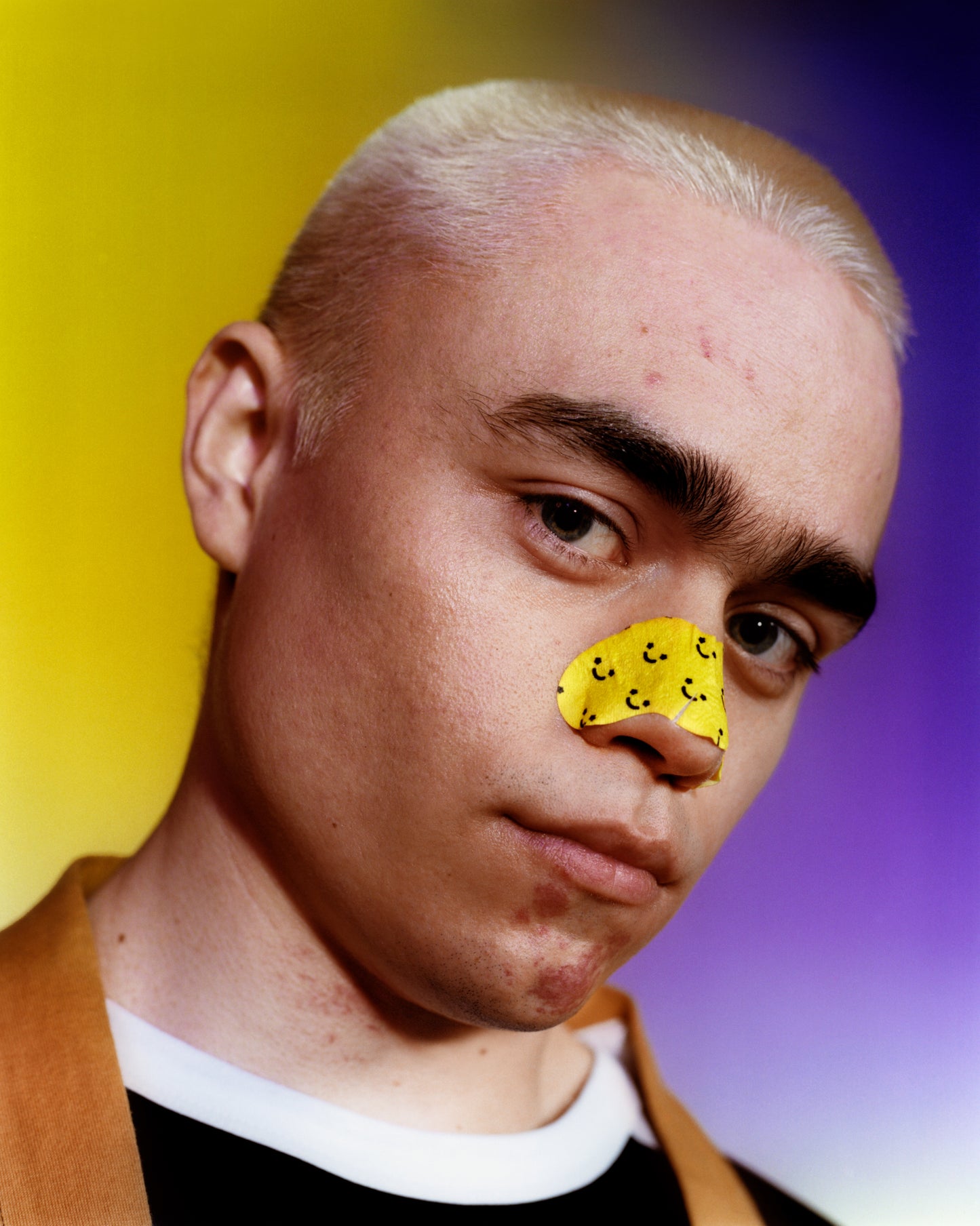 Young model with blonde buzz cut wears a Starface Lift Off Pore Strip which contains aloe vera extract across their nose to instantly unclog pores.