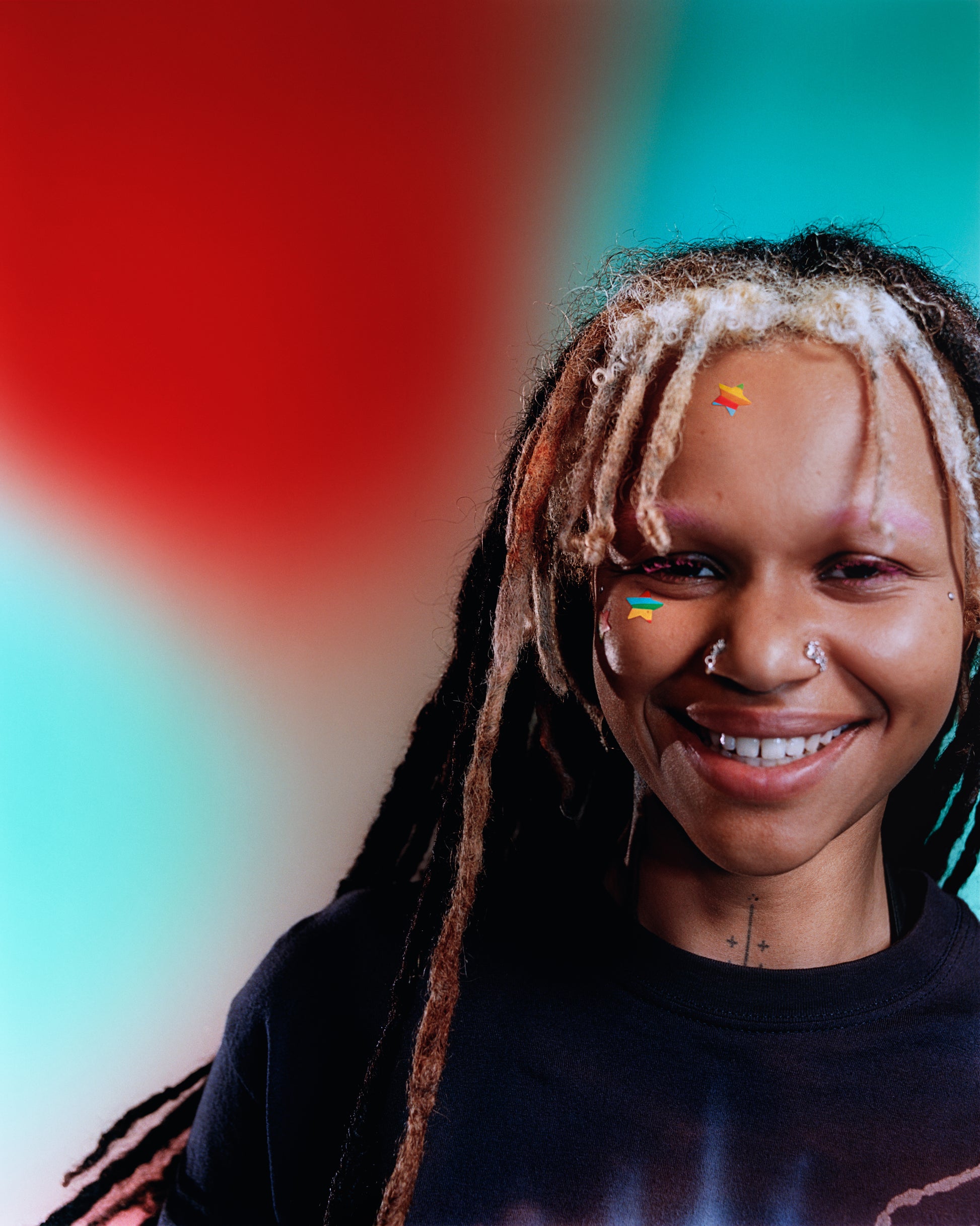 Close-up of a young model smiling and wearing a Starface Rainbow Star hydrocolloid pimple patch on their cheek and forehead.
