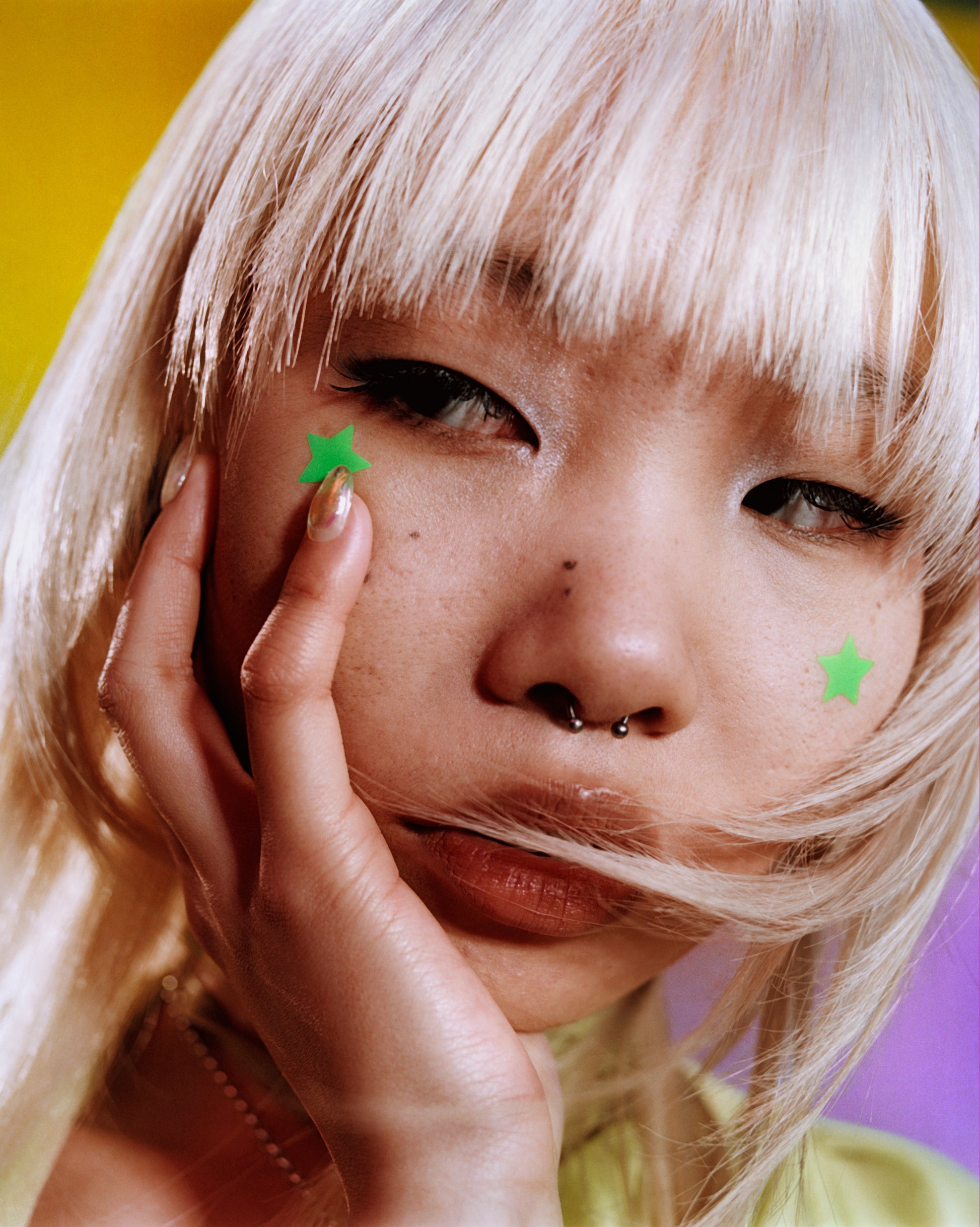 A young person with blonde hair wears green Starface Hydro-Star® + Tea Tree star-shaped patches on both sides of their cheeks.