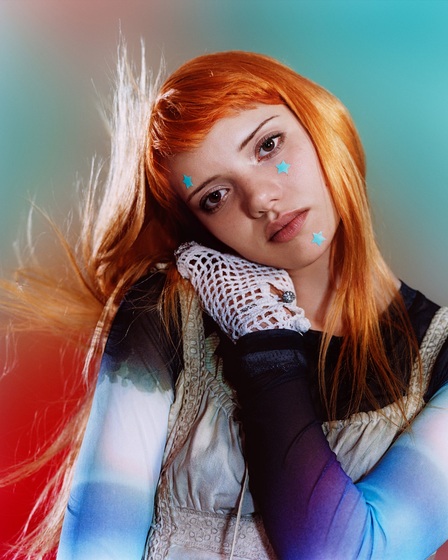A young person with long red hair wears blue Hydro-Star® + Salicylic Acid star-shaped pimple patches on their chin, under eye area, and forehead.