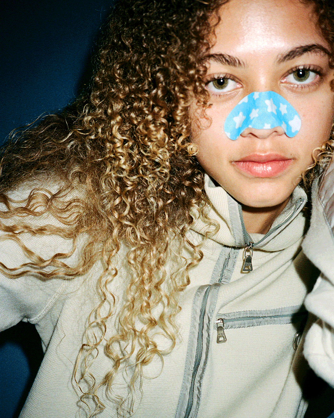 A person wearing a blue Starface Star Strips™ + Salicylic Acid pore strip on their nose. Pore strips that lift away buildup.